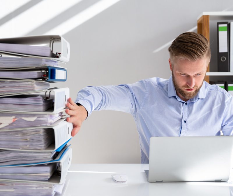 Man at desk pushing away paper document and switching to digital documents on a laptop