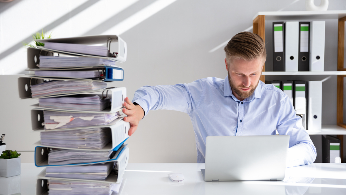 Man at desk pushing away paper document and switching to digital documents on a laptop