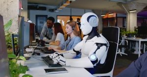 Robot working at computer among people. Machine typing on keyboard in office. IT team of future. Futuristic technology.