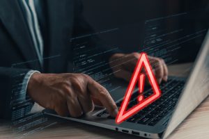 A professional uses a laptop displaying a glowing red warning triangle with an exclamation mark, symbolizing caution and cybersecurity threats. Unsupported operating software.