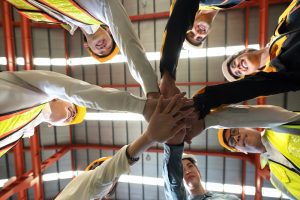 Group of male and female factory labor join hands together after finish meeting. Support of cybersecurity culture in manufacturing.